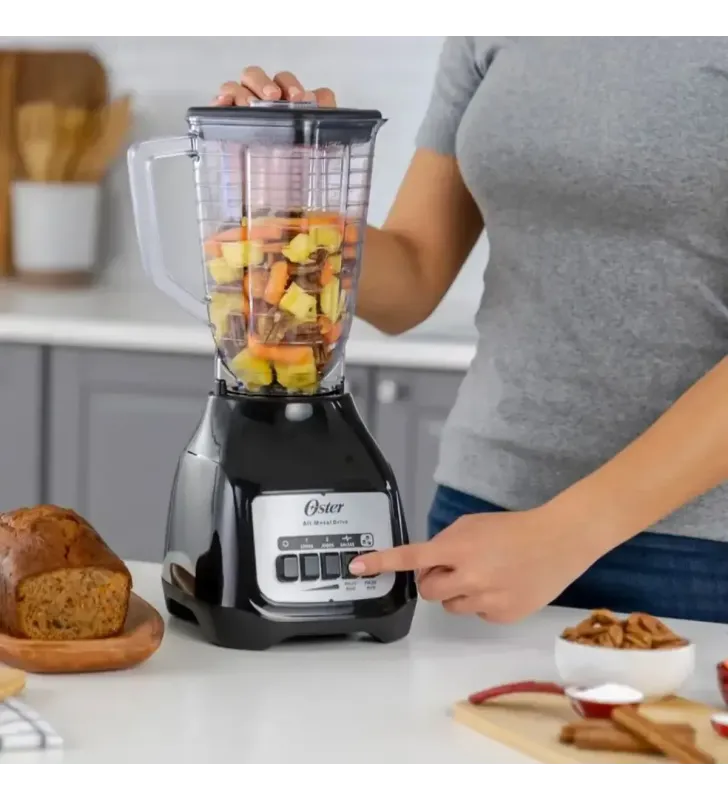 Licuadora Oster Kaliman negra con vaso plástico transparente y frutas dentro, base con botones blancos.