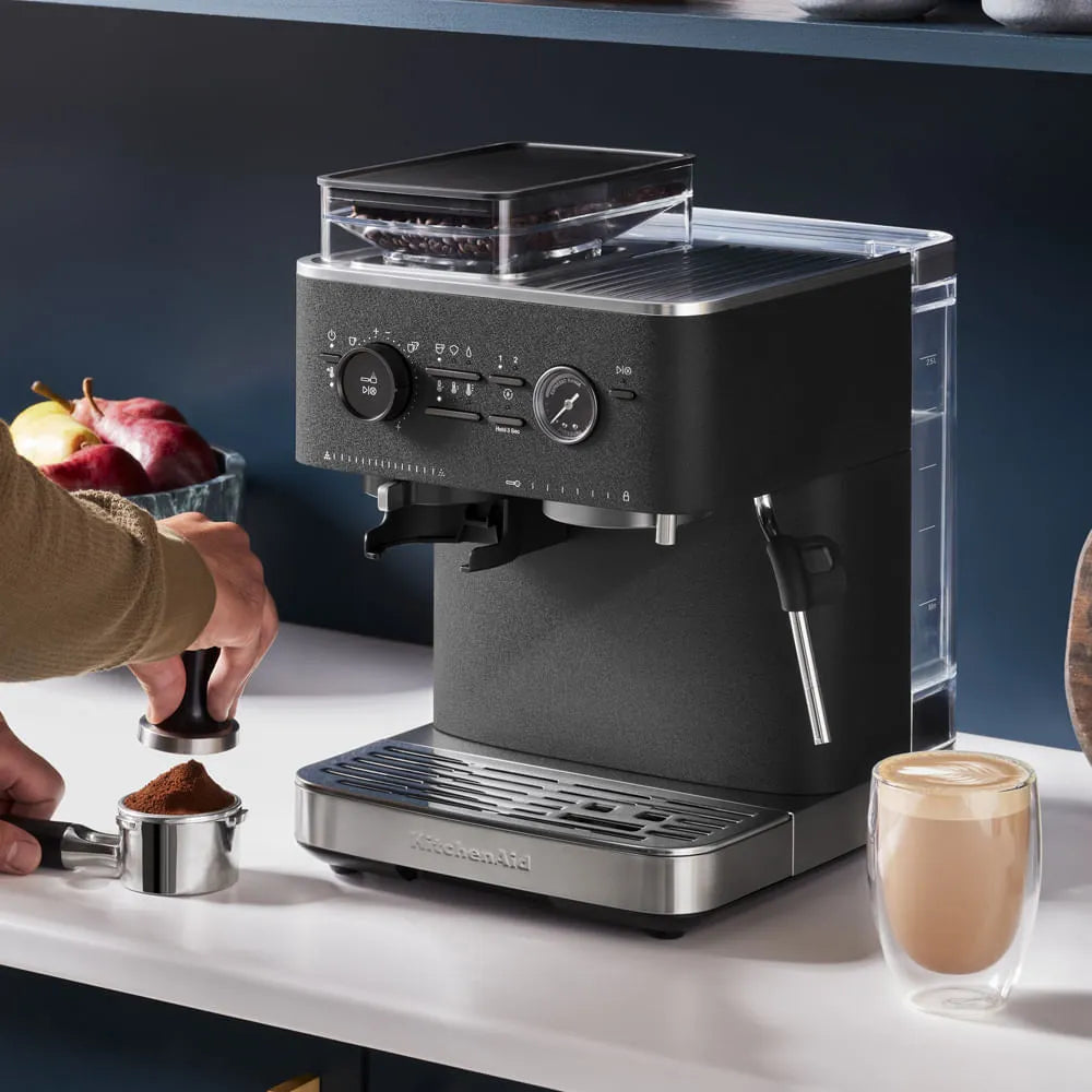 Cafetera semiautomática KitchenAid negra con molinillo integrado y vaporizador de leche, estilo industrial.