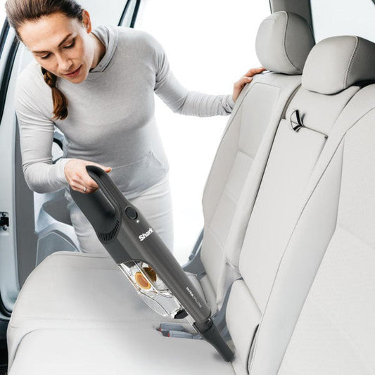 Aspiradora de mano inalámbrica Shark UltraCyclone negra limpiando asiento de coche gris claro.