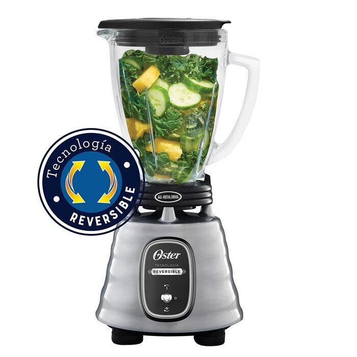 Licuadora Oster 700W base acero inoxidable con vaso de vidrio y tapa negra, llenado con frutas y verduras verdes.