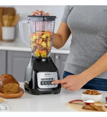 Licuadora Oster Kaliman negra con vaso plástico transparente y frutas dentro, base con botones blancos.