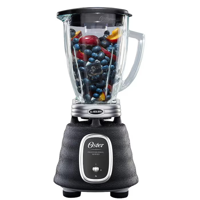 Licuadora Oster negra con base texturizada, vaso de vidrio transparente lleno de frutas frescas.