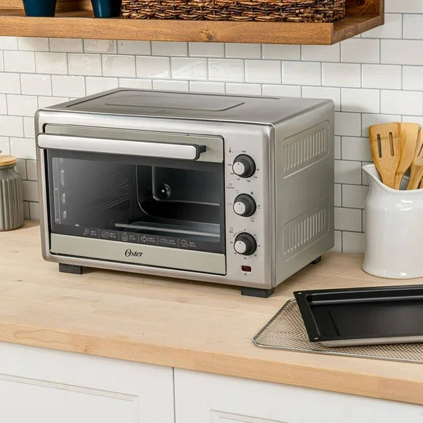 Horno eléctrico Oster color gris con puerta de vidrio y tres perillas frontales sobre encimera de cocina blanca.