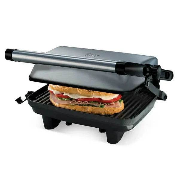 Sandwichera compacta Oster de acero inoxidable con parrilla antiadherente y manija negra, sandwich tostado visible.
