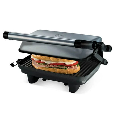 Sandwichera compacta Oster de acero inoxidable con parrilla antiadherente y manija negra, sandwich tostado visible.