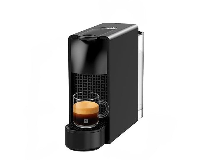 Cafetera Nespresso Essenza Mini negra ultra compacta con vaso de espresso y espuma crema visible.