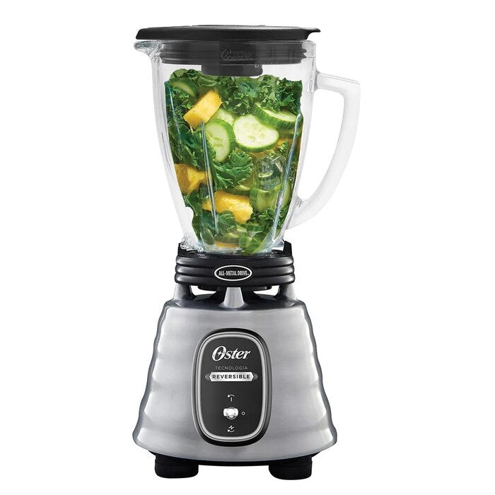 Licuadora Oster acero inoxidable 700W con vaso de vidrio y tapa negra con frutas y verduras en su interior.