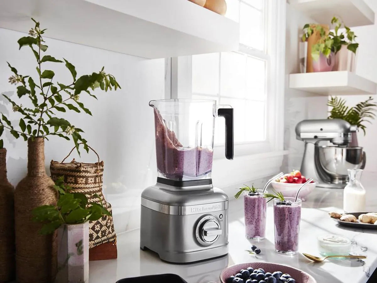 Licuadora KitchenAid K400 gris metálico con jarra transparente y batido morado dentro en cocina blanca moderna.